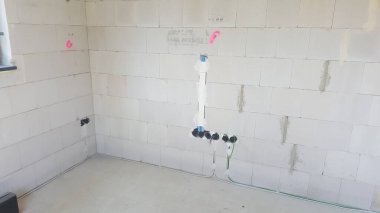 Beton blok duvarları, açıkta kalan elektrik hatları ve boruları tamamlamaya hazır olan tamamlanmamış bir binanın içi.