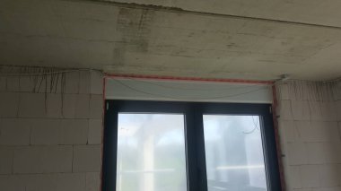 Tamamlanmamış beton tavan ve elektrik kabloları ve pencere çerçevesi kurulumuyla tuğla duvarlar