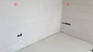 Beyaz tuğla duvarlı tamamlanmamış oda, açıkta bırakılmış elektrik kutuları ve kuruluma hazır kablolar.