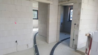 Bir evin tamamlanmamış iç kısımlarında zemine ve duvarlara döşenmiş elektrik kabloları ve borularıyla hafif beton bloklardan yapılmış duvarlar bulunuyor.