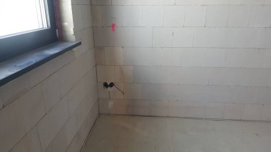 İnşaat halindeki bir iç mekan, havalandırılmış beton blok duvarlar, karanlık bir pencere pervazı ve kablolu elektrik prizleri.
