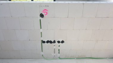 Beton bloklardan yapılmış bir duvarda yeni kurulmuş elektrik kabloları ve bağlantı kutuları görülüyor.