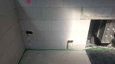 Beton blok duvarlı tamamlanmamış iç alan, görünür elektrik hatları, ve kabataslak döşeme, devam eden bina veya yenileme çalışmalarını gösteriyor