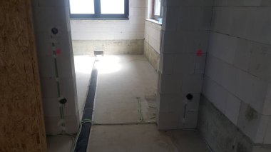 Beton zemin, beton blok duvarlar ve görünür elektrik kabloları ve elektrik kabloları ile tamamlanmamış iç alan, devam eden bina veya yenileme çalışmalarını gösteriyor