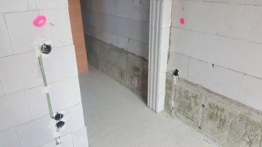 Görünür elektrik hatları, prizleri, ham beton ve blok duvarları olan tamamlanmamış iç alan, devam eden bina veya yenileme çalışmalarını gösteriyor