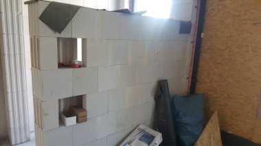 Hafif beton bloklardan kısmen inşa edilmiş bir duvarı gösteren bir inşaat sahasının iç görüntüsü. Bölgeye çeşitli yapı malzemeleri saçılmış.