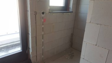 İnşaat halindeki bir binanın iç görüntüsü, elektrik kabloları ve pencere çerçevesi için kanalları olan ham beton blok duvarları gösteriyor.