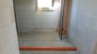 İnşaat halindeki bir odada beton, tuğla duvarlar ve bir pencere var. Gelişmeyi ve son rötuşları bekliyor.