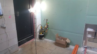 A view of an unfinished room with plumbing pipes, drywall, and a door, indicating ongoing construction or renovation work