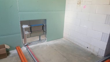 Tadilattan geçen bir odada görünür bir tesisat manifoldu sistemi ve metal bir çerçeveye kısmen yerleştirilmiş beton zemin ve beton blok duvarlı alçıpan bulunuyor.