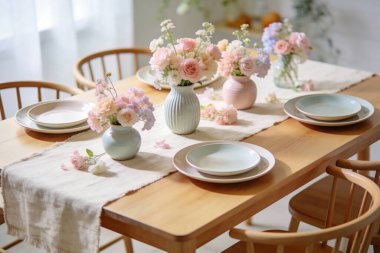 Güzelce düzenlenmiş bir yemek masasında, yumuşak doğal ışıkla yıkanmış, tabaklar ve keten koşucuyla hazırlanmış, küçük vazolar halinde pastel renkte çiçekler bulunur.
