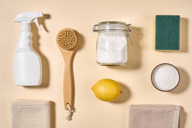 Sprey şişe, ahşap fırça, kabartma tozu, limon, sünger ve havlu gibi çevre dostu temizlik malzemelerinden oluşan düz bir düzenleme.