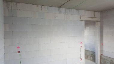 Hafif havalandırmalı beton bloklardan inşa edilmiş duvarlar, görülebilir elektrik hatları ve gelecekteki kurulumlar için işaretlerle tamamlanmamış iç uzay