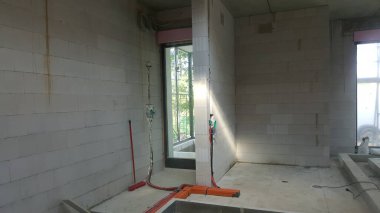 Tamamlanmamış iç mekan, işlenmemiş tuğla duvarlar, görünür elektrik hatları ve devam eden bina ve yenileme çalışmalarını gösteren geniş bir pencere.
