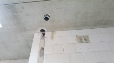 İnşaat halindeki bir binanın tamamlanmamış iç kısmı beton bir tavan, borular ve beyaz beton bloklardan yapılmış duvarlar gösteriyor.