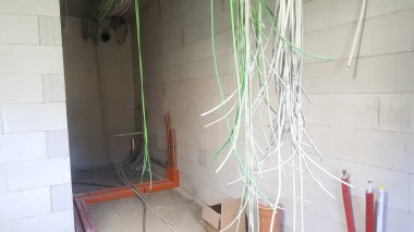 Bitmemiş duvarları, açıkta kalmış elektrik kablolarını ve tesisat borularını gösteren bir inşaat alanının iç görüntüsü kuruluma hazır.