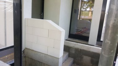 İnşaat halindeki bir evin dış görünüşü, duvar binasının ilerlemesini gösteriyor. Hafif beton bloklar ve tamamlanmamış beton adımlarla.