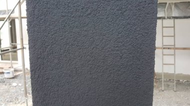 Koyu gri bir duvar yüzeyinin ayrıntılı bir görüntüsü, bir inşaat projesi sırasında dış sütundaki tanecikli dokusu ve uygulamasını gösterir