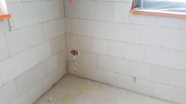 Havalandırma beton duvarlı tamamlanmamış iç mekan, açıkta duran elektrik kutuları, ve yerde görünen kablolar, devam eden inşaat çalışmalarını gösteriyor.