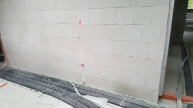 Hafif beton bloklardan yapılmış bir duvar yapım aşamasında ve yerde elektrik kabloları ve kanalları var.
