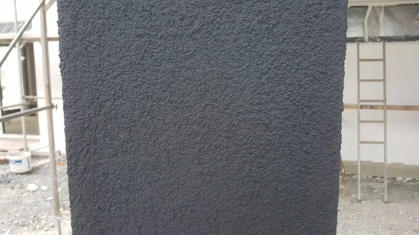 Koyu gri bir duvar yüzeyinin ayrıntılı bir görüntüsü, bir inşaat projesi sırasında dış sütundaki tanecikli dokusu ve uygulamasını gösterir
