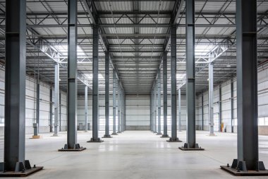 Geniş, modern depo alanı. Beton zemin, metal çatı yapısı ve geniş giriş kapıları var. Depolama ve dağıtım işlemleri için hazır.