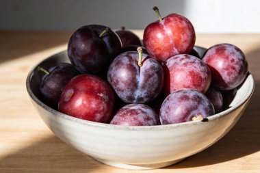 Koyu mor ve kırmızı eriklerle dolu seramik bir kasenin yakın plan görüntüsü, noktalı ışığın altında doğal dokularını ve canlı renklerini sergiliyor.