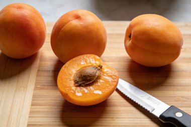 Çok sayıda kayısı ve tohumlarını gösteren yarım kayısı yakın plan bir çekim, yakınlarda tırtıklı bir bıçakla ahşap bir yüzeye yerleştirilir.