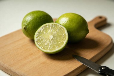 Canlı yeşil limonların yakın plan görüntüsü. İçi sulu, küçük bir bıçağın yanındaki doğal bir tahta kesme tahtasının üzerinde duruyor.