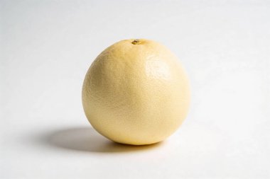 Açık sarı kabuklu, soyulmamış bir greyfurt parlak beyaz bir yüzey üzerine kuruludur.