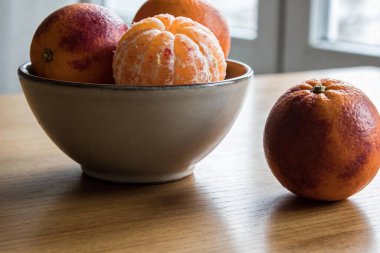 Kanlı portakallarla dolu seramik bir kasenin yakından görüntüsü, ahşap bir yüzey üzerinde kasenin yanına yerleştirilmiş tam bir kan portakalı.