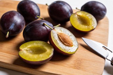 Bir sürü koyu mor erik, parlak sarı et ve küçük bir bıçağın yanındaki bambu kesme tahtasına bir çukur yerleştirilir.