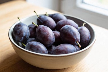 Koyu mor eriklerle dolu bir kasenin yakın plan görüntüsü pürüzsüz derilerini ve saplarını sergiliyor, yumuşak doğal ışıkla yıkanmış.