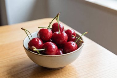 Işıl ışıl, koyu kırmızı kirazlarla dolu bir kasenin yakın plan görüntüsü, canlı renkleri ve taze sapları sergileniyor.
