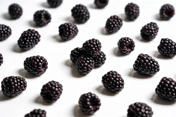 Olgun, koyu böğürtlenlerden oluşan bir koleksiyon parlak beyaz bir arkaplana yerleştirilmiş, görsel olarak çekici bir desen oluşturuyor.