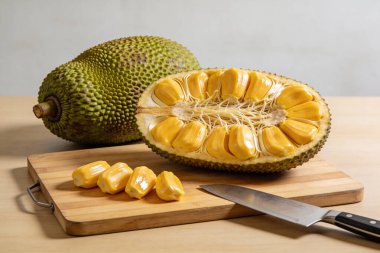 Koca bir Jackfruit yarı yarıya bir tanesinin yanında oturuyor, canlı sarı kapsüllerini ve ince çekirdeklerini gösteriyor, hazırlanmaya hazır.