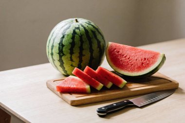 Bütün bir karpuz, yakınlarda bir bıçakla birlikte tahtada sulu dilimler ve karpuz çubuklarının yanında durur.