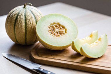 Olgun bir kavun ikiye bölünür ve bambu kesme tahtasıyla dilimlenir. Yanında şef bıçağıyla servis yapmaya hazırdır.