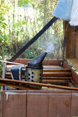 Bir arı yetiştiricisinin başlıca içicisi açık bir arı kovanına dayanır, arka bahçedeki arı kovanının kırsal cazibesinin ortasında, arıcılık araçlarını ve kovan yapılarını sergileyerek, arı yetiştirme sürecini çağrıştıran bir his uyandırır..