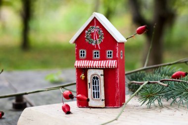 Hoş bir minyatür kırmızı oyuncak evi, çelenk ve ilginç detaylarla süslenmiş, doğal bir arka plana karşı bayram neşesini ve bayram neşesini sembolize eden, sıcaklık ve nostalji duygusu yaratan..