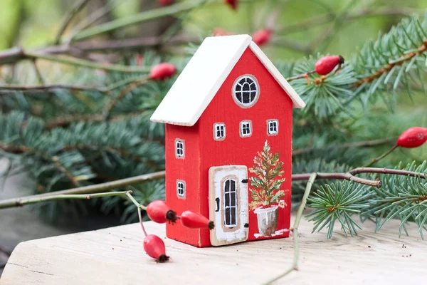 Beyaz çatılı, el boyası kırmızı ahşap bir evin enfes bir yakın çekimi. Noel ağacı tasarımı, doğal yeşillik ve kırmızı böğürtlenlerle çevrelenmiş, sıcak bir tatil ruhunu çağrıştırıyor..