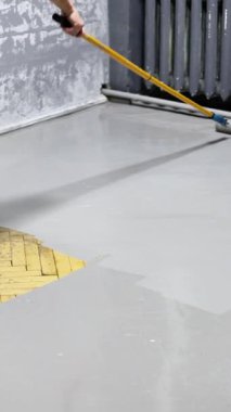 Ahşap bir zemine gri boya sürmek için boya silindiri kullanan, odanın görünümünü güncelleyen ve orijinal sarı döşeme tahtalarını kapatan birinin yakın çekim görüntüsü. DIY projesi alanı geliştirir.