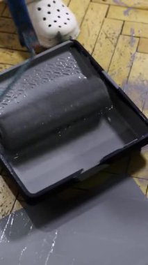 Gri boyaya batırılmış, tablasında hazır bir boya rulosu yakalamak, ev yenilemelerini, DIY projelerini veya boyama sürecini resmetmek için ideal, arka planda beyaz bir tıkanma ile tamamlanmış..