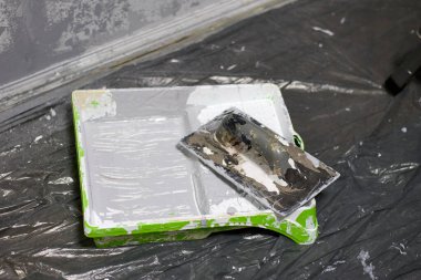 Gri boyalı yeşil boya tepsisinin yakın çekimi ve plastik bir çarşafta boyayla kaplanmış bir boya silindiri, ev yenileme ve tasarım geliştirme amaçlı bir duvar boyası projesini resmediyor..