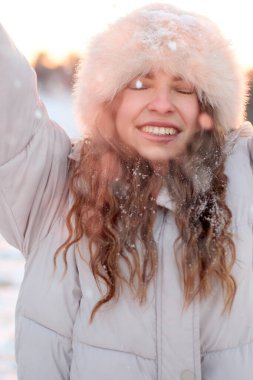 Keyifli, genç bir kadının hoş bir yakın çekimi rahat bir kürk şapkası ve kışlık ceketi, güneşli bir günde güneşlenirken, sıcaklık ve mutluluk yayarken, kış mevsimi promosyonları için mükemmel..