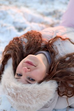 Huzurlu bir portre, parlak bir kış günü, kar üzerinde huzur içinde yatan genç bir kadını yakalar. Kırmızımsı kahverengi saçları beyaza doğru yayılmış, sıcak bir kürk şapka takmış ve doğrudan kameraya bakar..