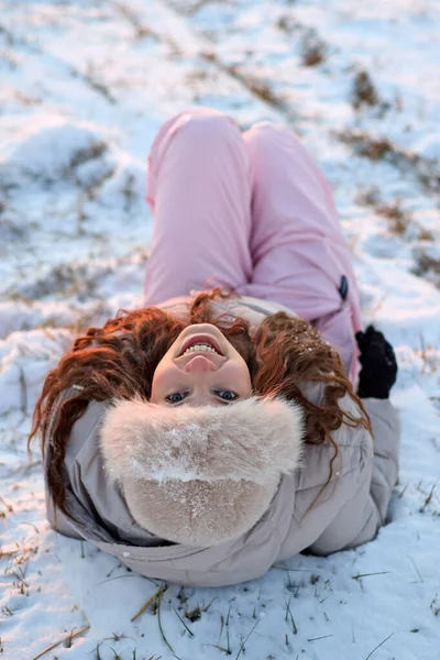 Karda sırtüstü uzanmış, kış gününün keyfini çıkartan neşeli genç bir kadın. Kürk şapkası ve güzel bir gülümsemeyle, rahat bir mevsim portresi yaratıyor..
