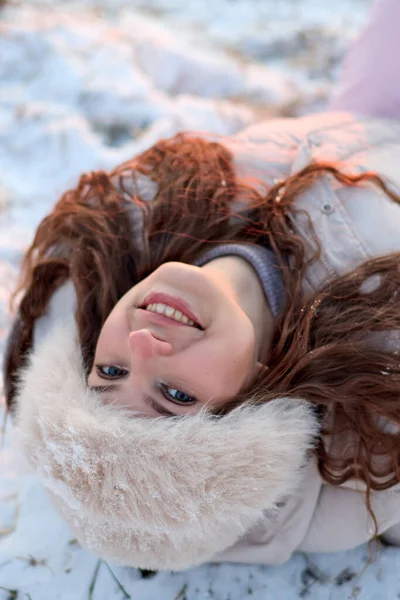 Kış günü kar altında yatan, uzun kıvırcık saçlı, kürk şapkalı, sevimli bir gülümsemeyle kameraya bakan, kışın güzelliğini yakalayan çekici genç bir kadın..