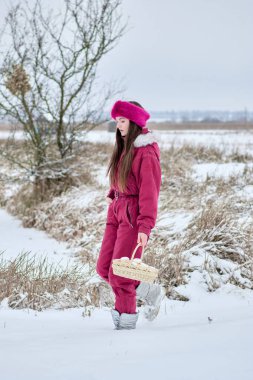 Pembe kar elbisesi giymiş ve pembe kürklü bir bantla beyaz yumurta dolu bir sepetle kar tarlasında yürüyen genç bir kadın, bir kış gününün dinginliğinin tadını çıkarıyor..