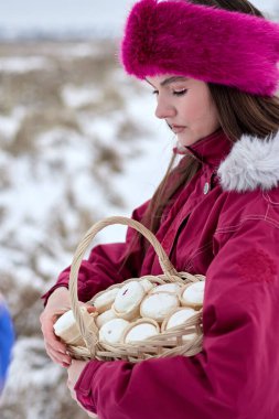 Pembe ceketli, kürklü ve saç bantlı çekici genç bir kadın. Karlı bir arazide içi dondurma külahlarıyla dolu örülmüş bir sepet taşıyor..
